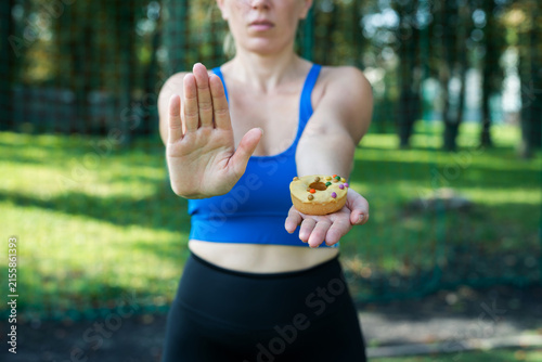 athletic woman holding donut dessert and showing refusal gesture,