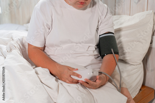 Fotografía A woman in a white T-shirt sits on the bed and measures her blood pressure and p