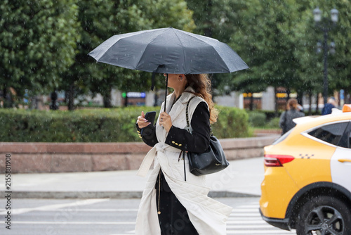 Woman with umbrella walking on city street on taxi car background, rainy weather