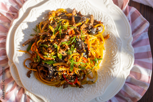 Asian wok stir fry noodles with beef and vegetables on wooden table