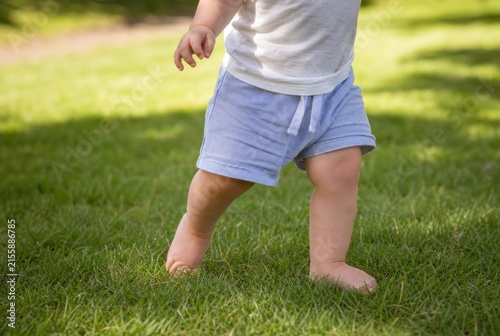Young toddler barefoot running excitedly on lush green grass in sunny outdoor park, playful childhood moment with vibrant light