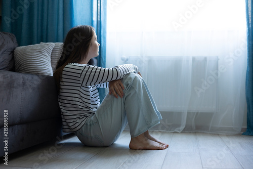 Fotografie Depressed teenage girl sitting alone at home, feeling sad and overwhelmed, menta