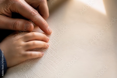 Child learning braille with parental guidance, hands on book, tactile reading in a supportive setting