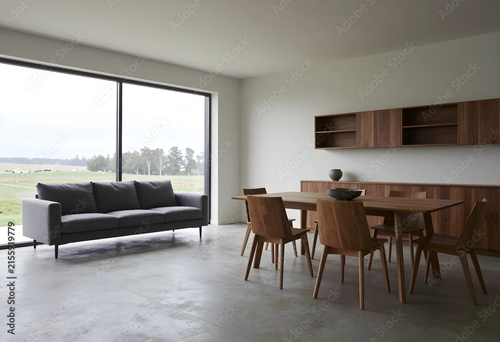 Fototapeta premium Modern minimalist living and dining room interior with large window overlooking a green landscape
