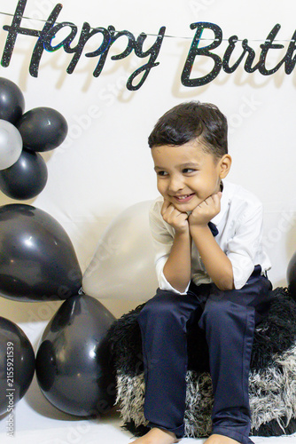 Cheerful Child Sitting On Chair During Birthday Celebration With Balloon Decor