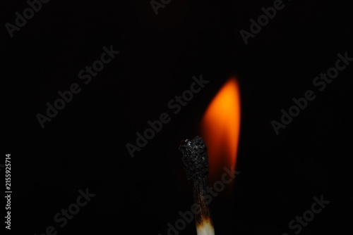 Close-up photograph of a burning match producing a soft orange flame against a completely dark background.