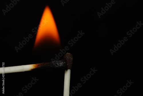 Extreme close-up macro photograph of a burning match surrounded by a large vivid orange and yellow flame against black.