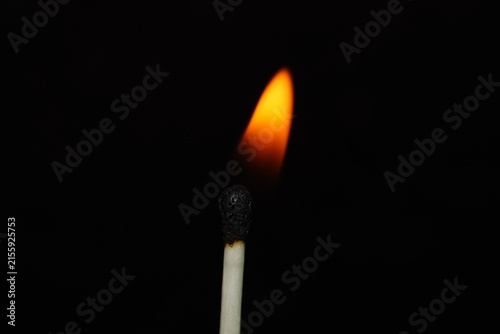 Minimal macro photograph of a completely charred matchstick with a faint orange glow behind it on a black background.