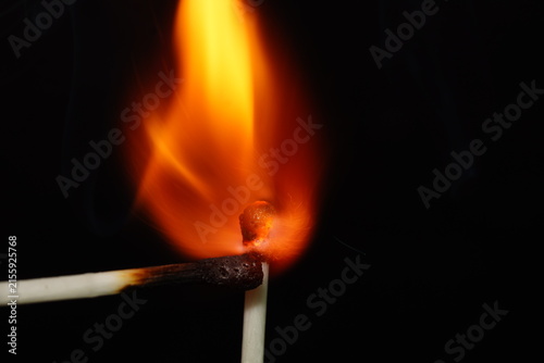 Dramatic macro photograph capturing the moment one burning match approaches another match, surrounded by an intense orange flame.