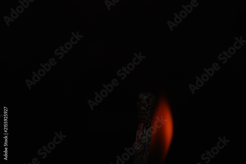 Moody macro photograph of a heavily burned matchstick silhouetted against a soft orange flame and dark background.
