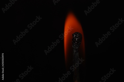 Minimal macro photograph of a single charred matchstick with a glowing orange flame isolated against black.