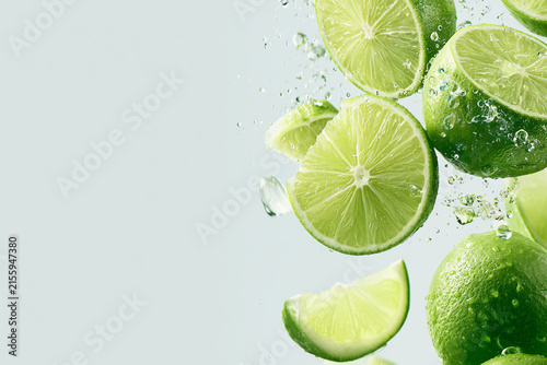 Fresh limes splashing in water with vibrant green color on a light background.