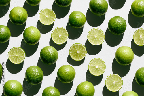 Vibrant green limes arranged creatively with shadows on a bright surface.