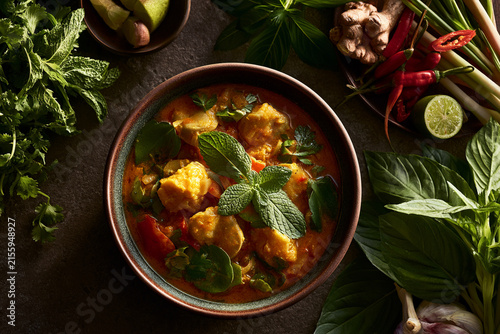 Delicious curry dish with fresh herbs and spices surrounding a colorful bowl.