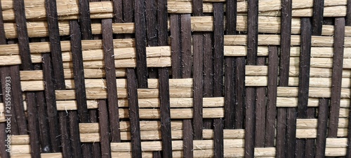 Close-up of a traditional two-tone woven bamboo or rattan pattern featuring alternating vertical black strips and horizontal natural tan, beige splints.It uses in traditional wall panels.