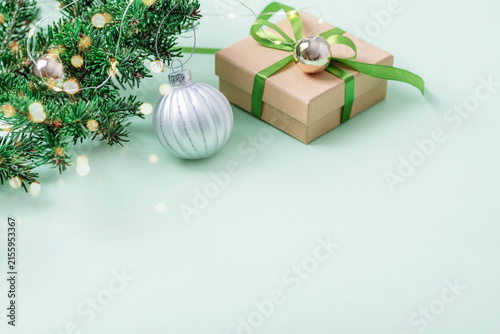 Christmas tree branches with silver ornament and wrapped gift box on green background with copy space. Top view