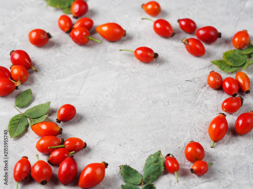 Foto Ripe red rose hips with green leaves on a gray concrete table , copy space