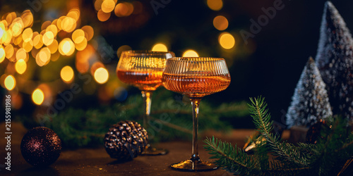 Stylish coupe glasses with sparkling rose wine on a festive holiday table surrounded by evergreen branches and warm Christmas lights, ideal for seasonal advertising, menus and invitations
