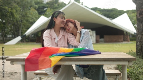 Canvas Print Affectionate Asian girls leaning towards each other tenderly over pride rainbow flag, expressing deep romantic love, joyful intimacy, and peaceful togetherness in public park setting
