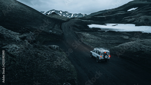 Cuadro en lienzo An off-road vehicle travels through the remote volcanic highlands near Mælifell, surrounded by black lava fields, lingering snow and dramatic mountain scenery in Iceland's untouched wilderness