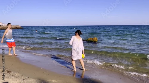 Mother and son experiencing sunny coastal resort lifestyle, playing ball in warm sea water during summer holiday. High quality FullHD footage