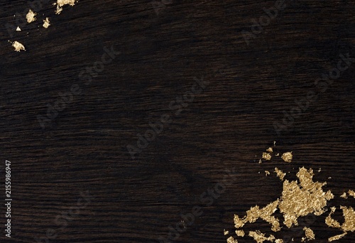 Dark wooden surface with gold leaf flakes scattered in corner texture