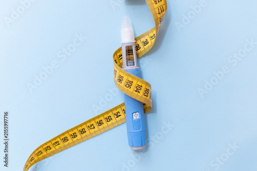 Bild auf Leinwand Top view of a medical injection pen tightly wrapped with a yellow measuring tape, symbolizing health risks of rapid weight loss, medication misuse, and dangerous focus on body measurements