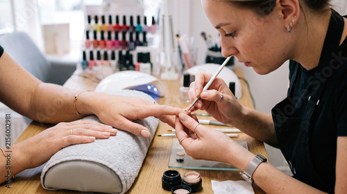 Professional manicurist carefully applying nail polish to a client's fingernail with a fine brush in a salon setting