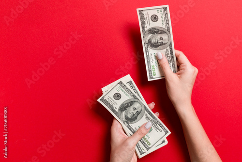 Female hand giving one hundred dollar banknotes on colorful background. Top view of wealth concept with empty space for your design