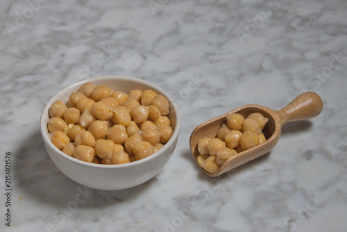 Cooked chickpeas with a wooden spoon on a marble table.