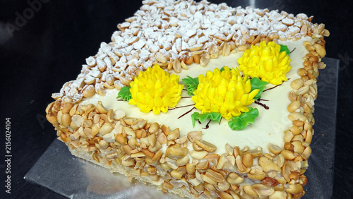 A beautifully decorated homemade cake, sprinkled with peanuts and powdered sugar, and topped with yellow buttercream flowers. A rustic, festive dessert for celebrations and special occasions.