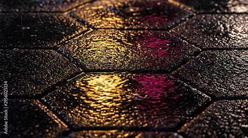 Wet hexagonal paving stones with vibrant yellow and pink reflections.