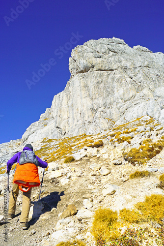 Fotografie Hiker ascending rocky trail toward monumental limestone formation on Bobotov Kuk route in Durmitor