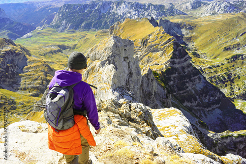 Canvastavla Traveler gazing from Bobotov Kuk peak at karst valley with isolated limestone spire, golden slopes, and distant summits
