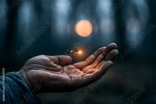 A hand holds a luminous firefly, radiating warmth in a dark, enchanting forest setting with bokeh lights.