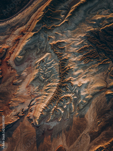 Bild auf Leinwand Layered ridges and winding channels form a dramatic geological landscape in brown and charcoal tones, creating an artistic natural texture shaped by erosion and time