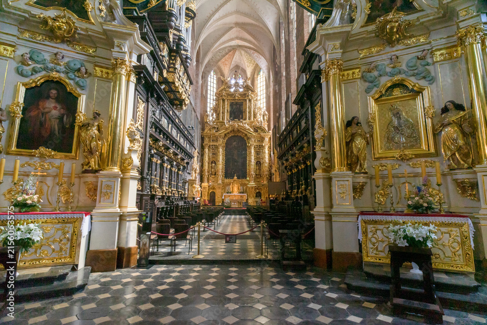 Fototapeta premium The magnificent high altar and dark wood choir stalls inside the 14th-century Corpus Christi Basilica in Kazimierz district of Kraków, Poland. A massive, highly ornate gold Baroque structure. 