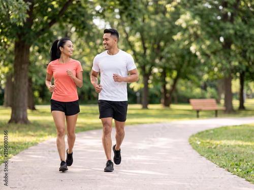 Young Southeast Asian couple jogging together in a green park for fitness wellness heart health relationship goals healthy lifestyle and outdoor exercise marketing