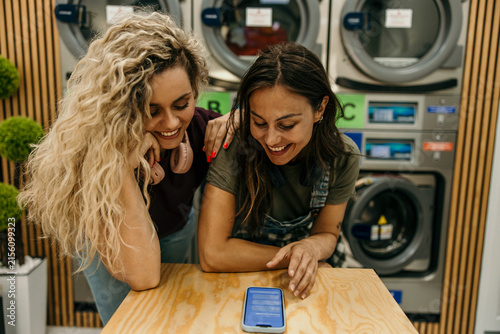 Friends using smartphone while waiting in laundromat