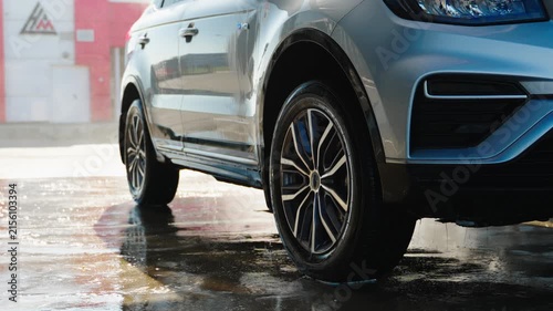 Silver SUV parked wet ground, raindrops gleam. Water drips from tire, reflecting red wall. Glossy paint catches light, showing sleek design. Perfect for car wash, automotive, or lifestyle ads