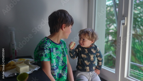 Принти на полотні Toddler sharing breakfast time with older brother by window creating heartwarmin