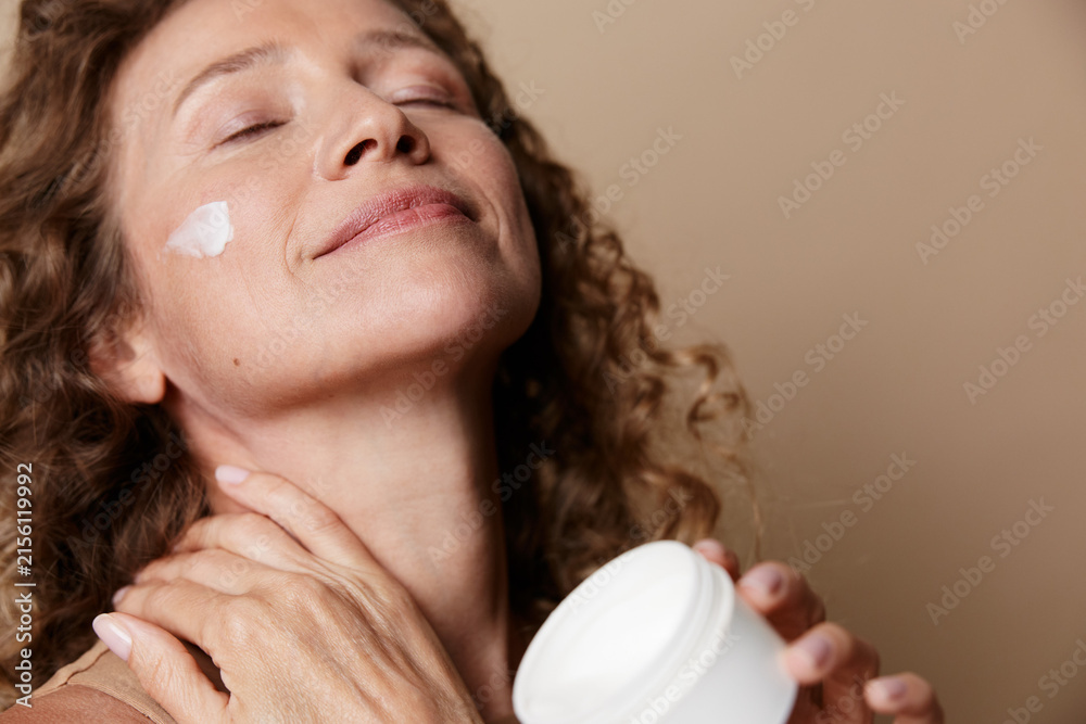 © SHOTPRIME STUDIO - A relaxed middle aged woman applies moisturizer on her face with eyes closed in a warmly lit room, highlighting natural beauty, selfcare, and authentic skin texture, calm confidence. © SHOTPRIME STUDIO - A relaxed middle aged woman applies moisturizer on her face with eyes closed in a warmly lit room, highlighting natural beauty, selfcare, and authentic skin texture, calm confidence.