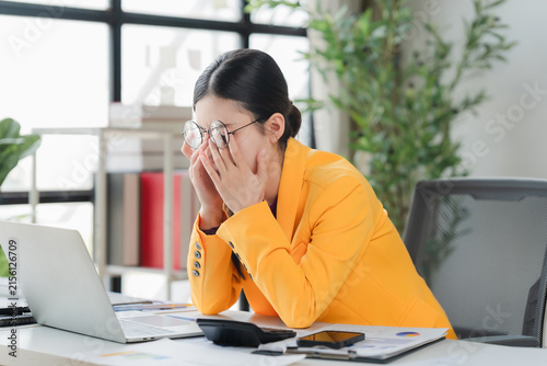 Фотография Concentrating on laptop, young woman experiences a sudden, painful headache