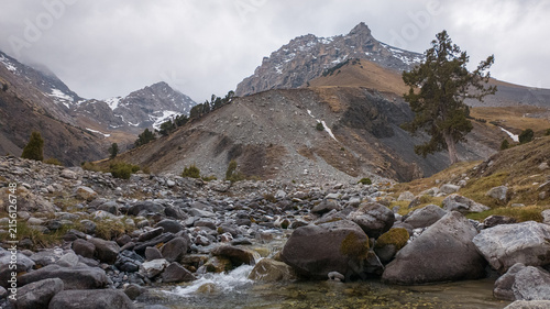 Cuadro en lienzo Rugged peaks rise in the background, with a clear stream flowing over smooth stones in the foreground