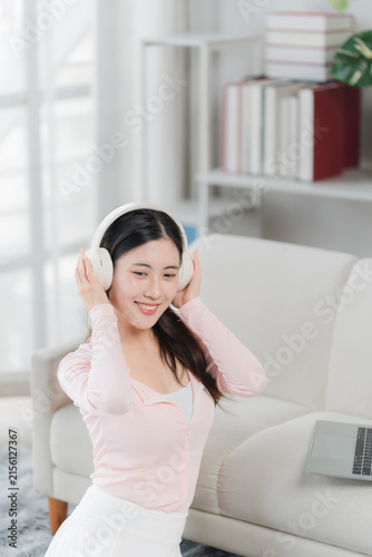 Cuadro en lienzo Joyful Melody: A young woman wearing headphones smiles warmly as she listens to music, enjoying a moment of relaxation and leisure at home