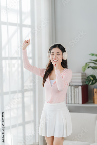 Obraz na płótnie Happy Girl Listening Music: A cheerful young woman with headphones on dances joyfully in a sunlit room, lost in the rhythm of her favorite song