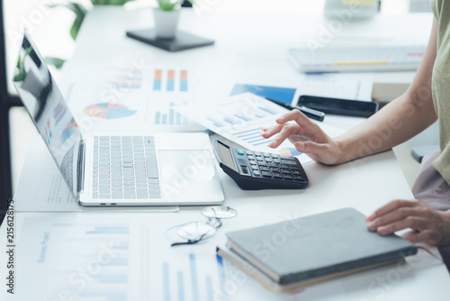 Fotografie Analyzing Financial Data: A person's hands are shown calculating numbers on a calculator with a laptop and financial charts on a desk, emphasizing financial analysis and accounting tasks