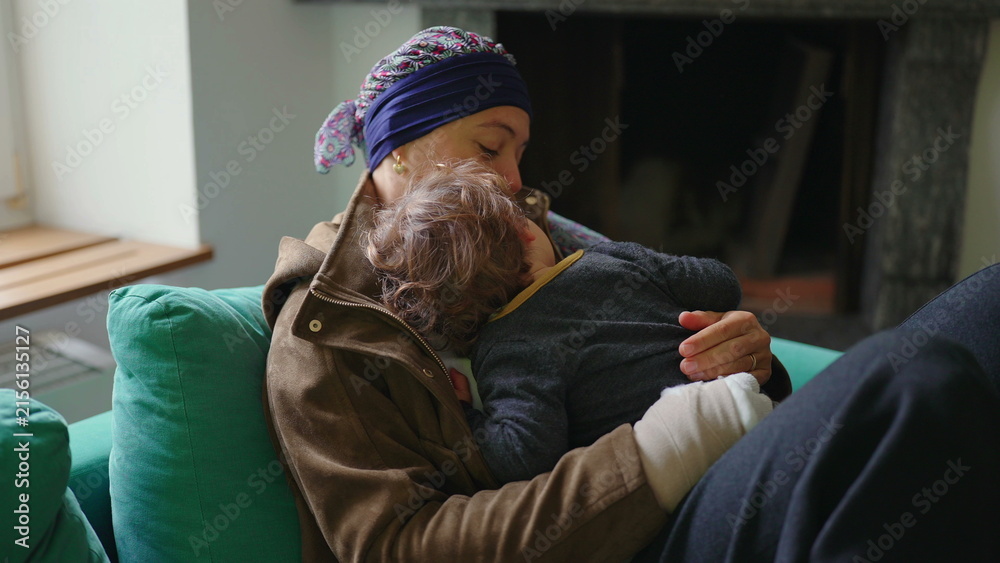 Fototapeta premium Mother recovering from cancer embracing toddler on sofa at home, family support moment highlighting healing, resilience, attachment and emotional strength