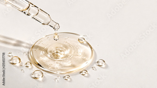 Transparent skincare serum and glass dropper with glossy liquid droplets on a clean white background, minimalist luxury beauty concept.