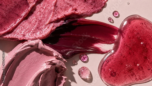 Rich berry skincare textures with pink exfoliating cream, deep burgundy gel and glossy red serum arranged on a soft blush background.